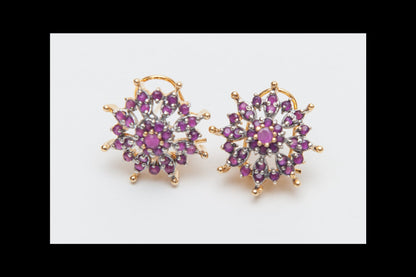 Pair of gold earrings with purple gemstones on a white background