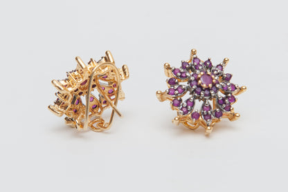 Pair of gold earrings with purple gemstones on a light gray background