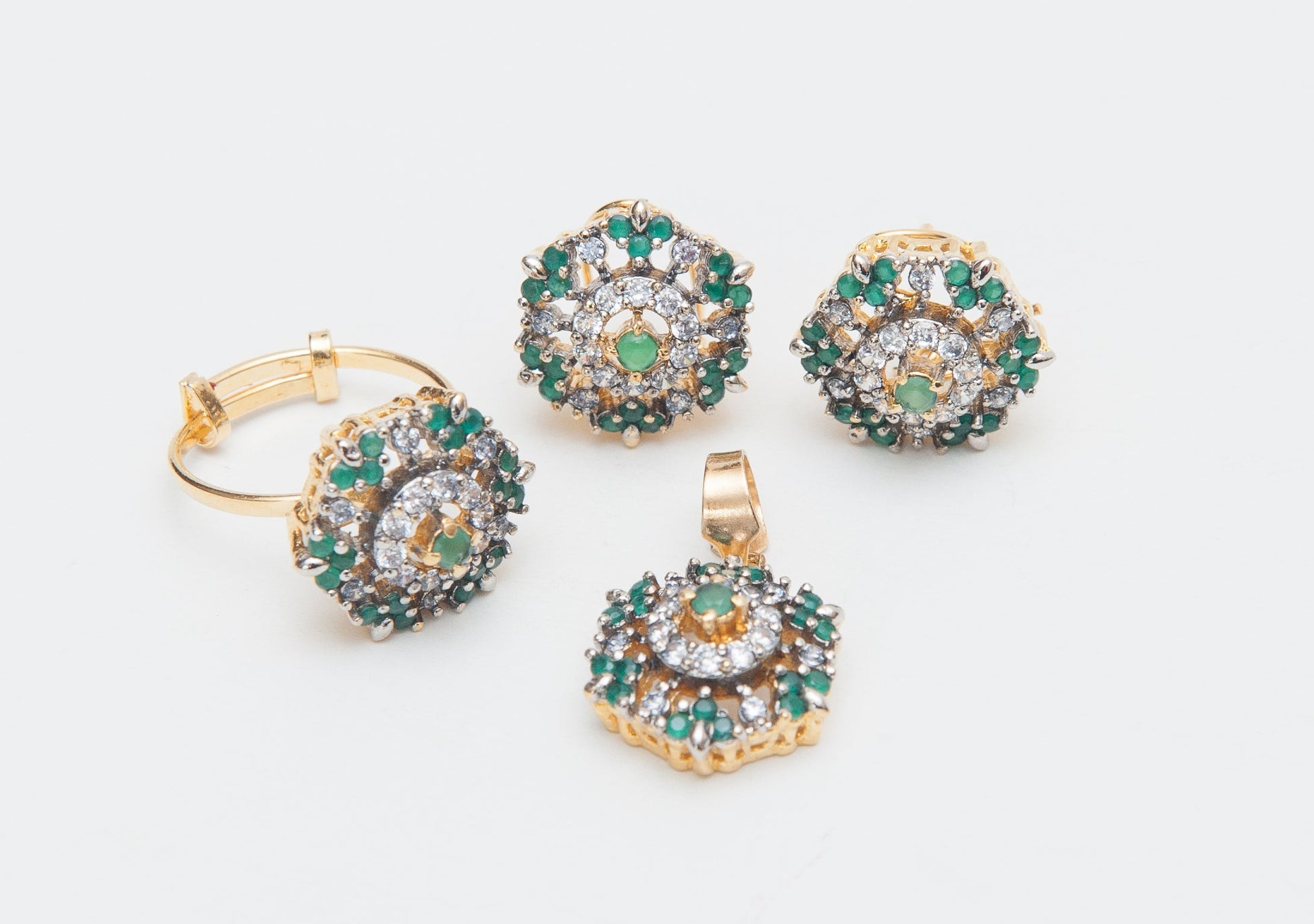 Gold jewelry set with emerald green stones on a white background