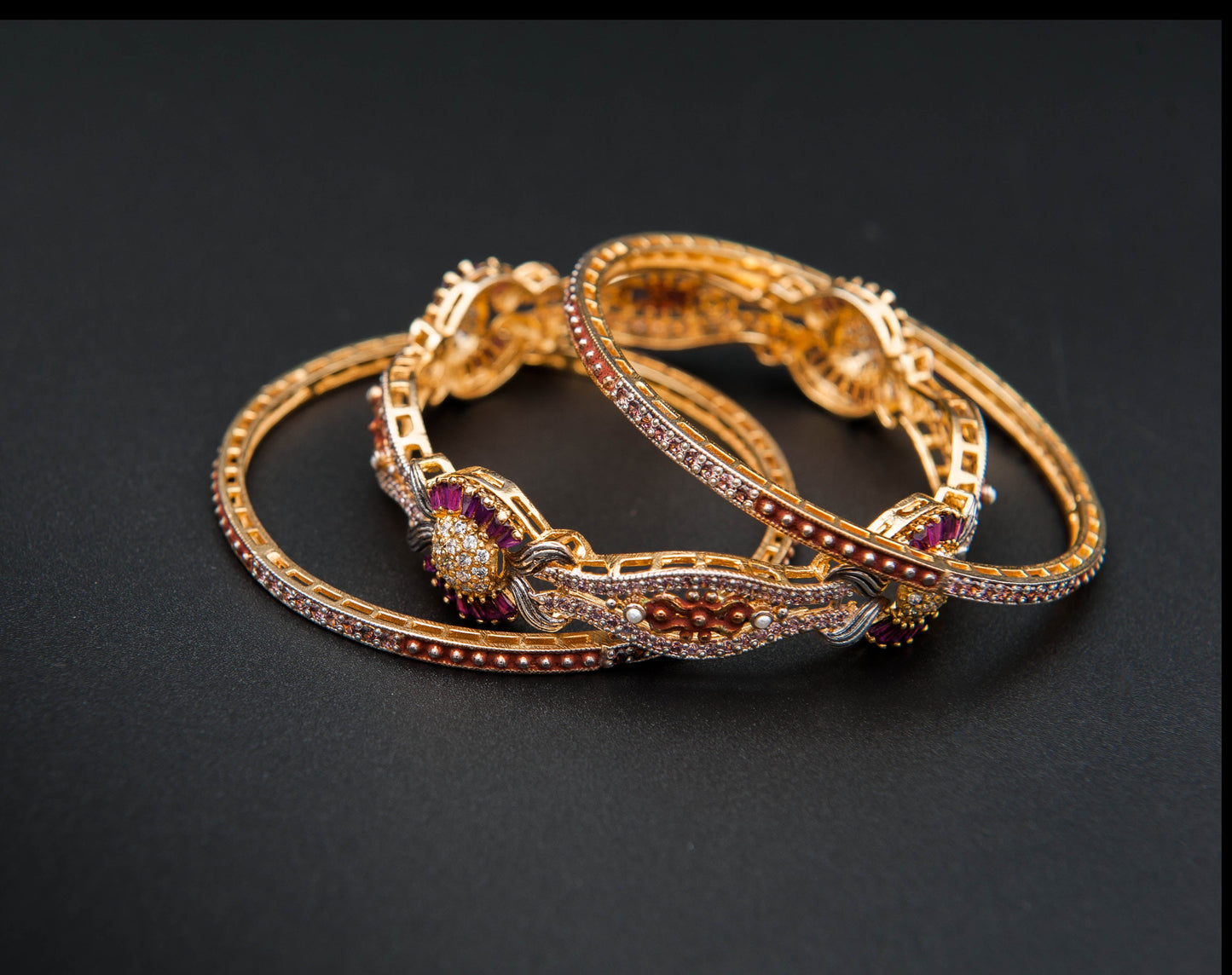 Pair of gold bracelets with gemstones on a black background