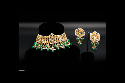 Gold and green jewelry set on black stands against a dark background